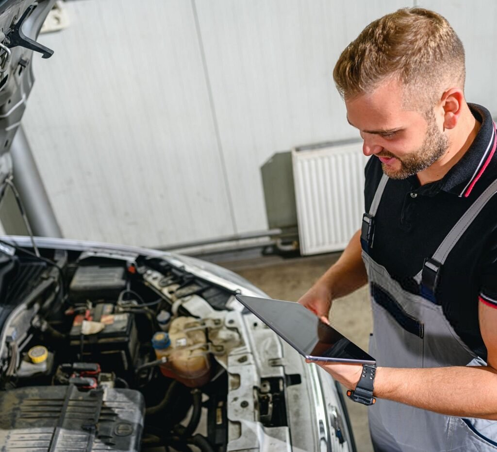 Mechanic using digital tablet in front of car hood in workshop