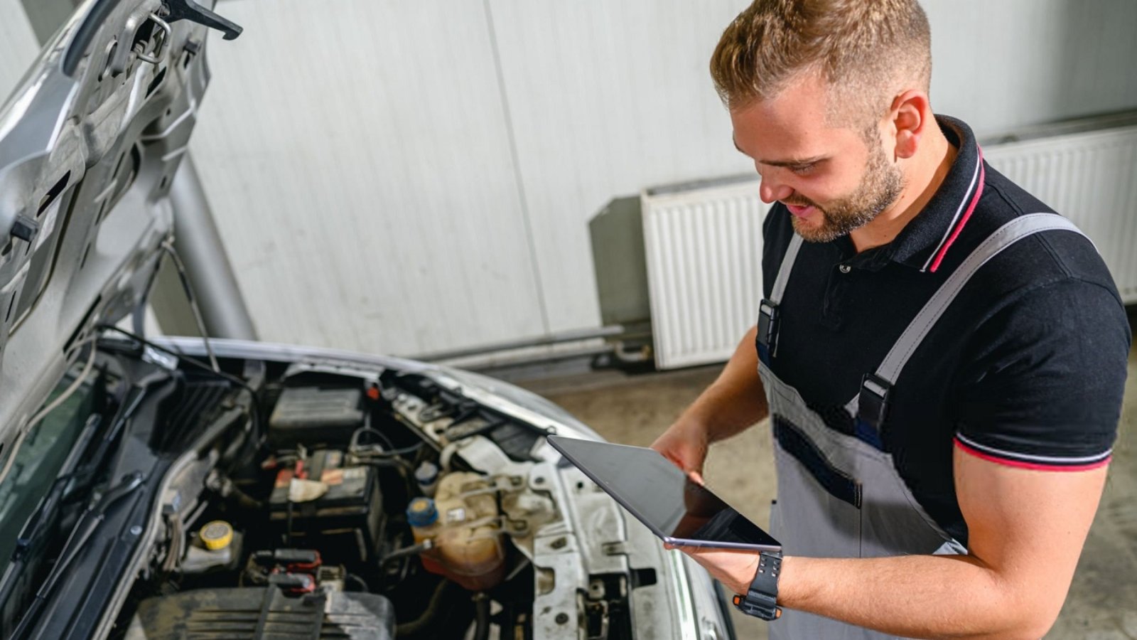 Mechanic using digital tablet in front of car hood in workshop