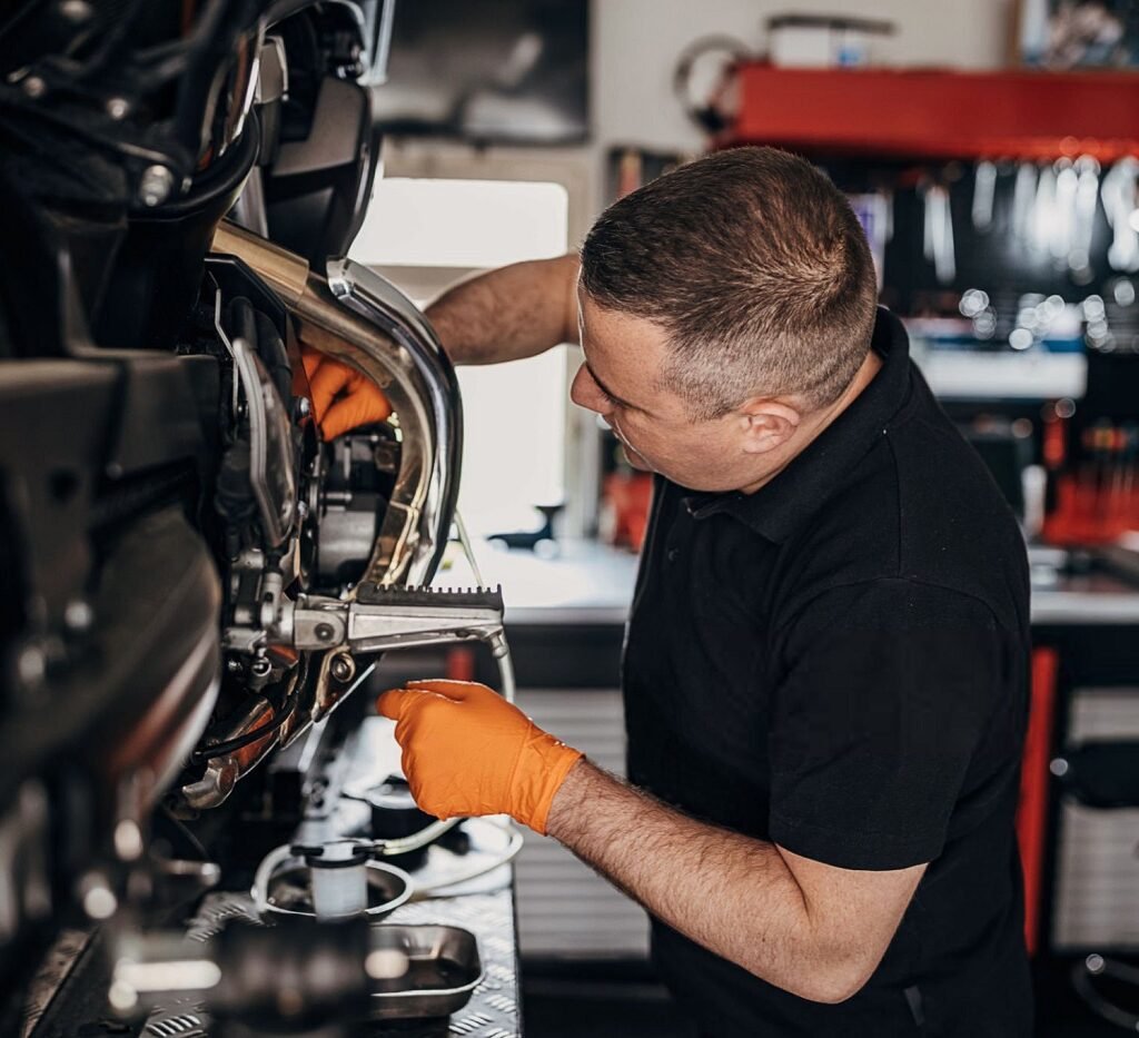 One man, male motorcycle mechanic inserting motor oil in motorcycle engine, in his workshop.