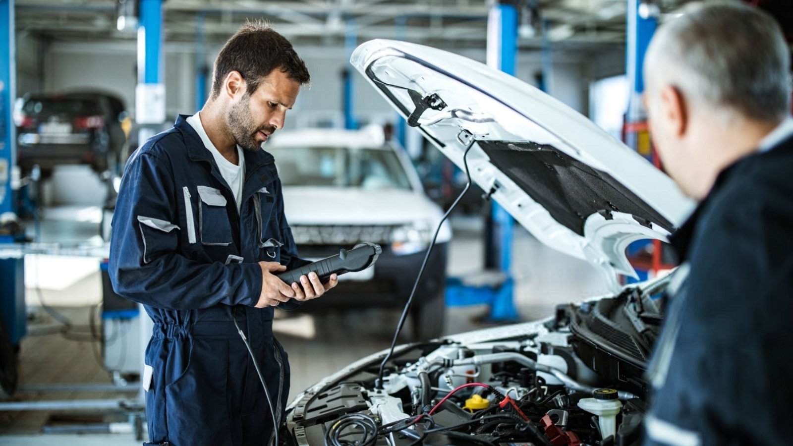 Young mechanic analyzing car's performance with diagnostic tool in a workshop.