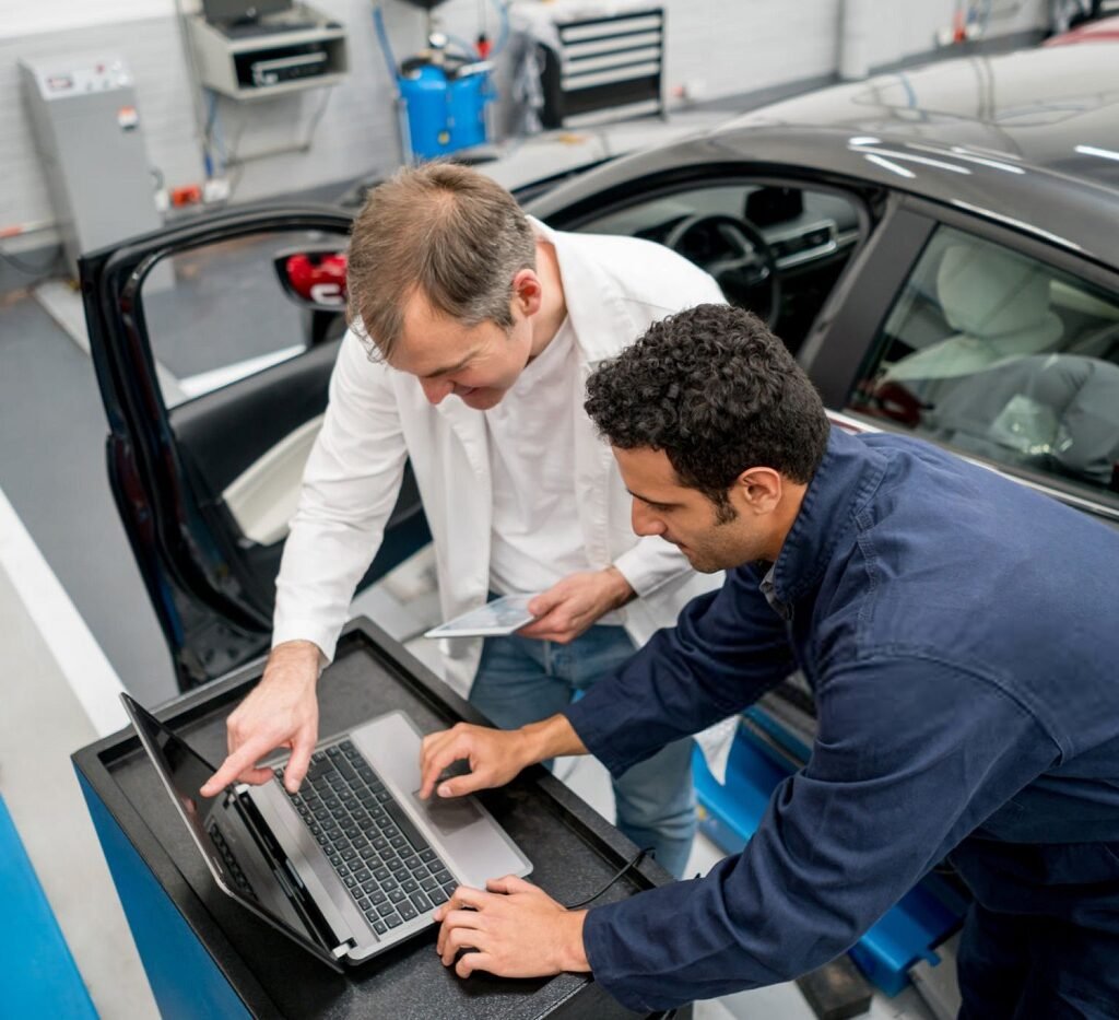 Team of mechanics working together at an auto repair shop using a computer to fix a car